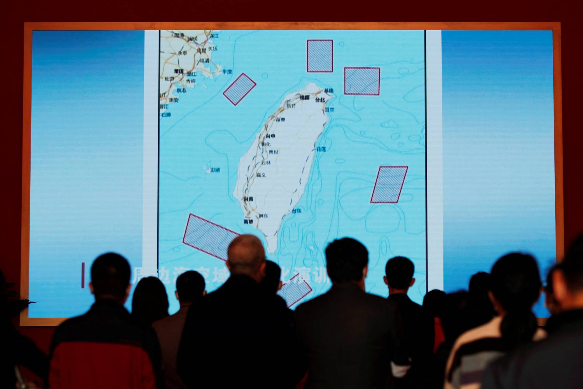 Visitors stand in front of a giant screen displaying a map of locations around Taiwan where the Chinese People's Liberation Army conducted military exercises in August, at an exhibition titled 'Forging Ahead in the New Era' during a media tour on Oct. 12, ahead of a Communist Party congress in Beijing this week. | REUTERS