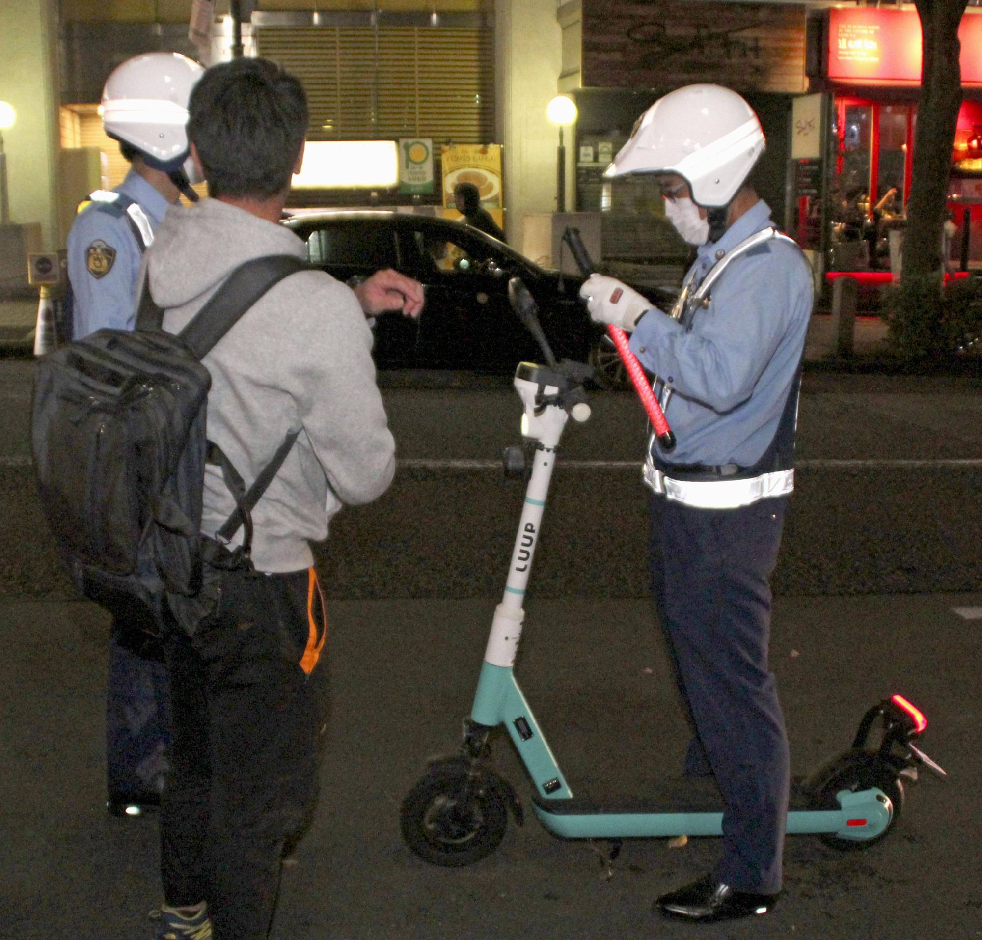 Police officers conduct an alcohol breath test on an electric scooter rider near Shibuya Station in Tokyo on Oct. 15. | KYODO