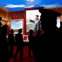 Chinese People\'s Liberation Army members walk past an image of Xi at an exhibition at the Military Museum in Beijing on Oct. 8. | REUTERS