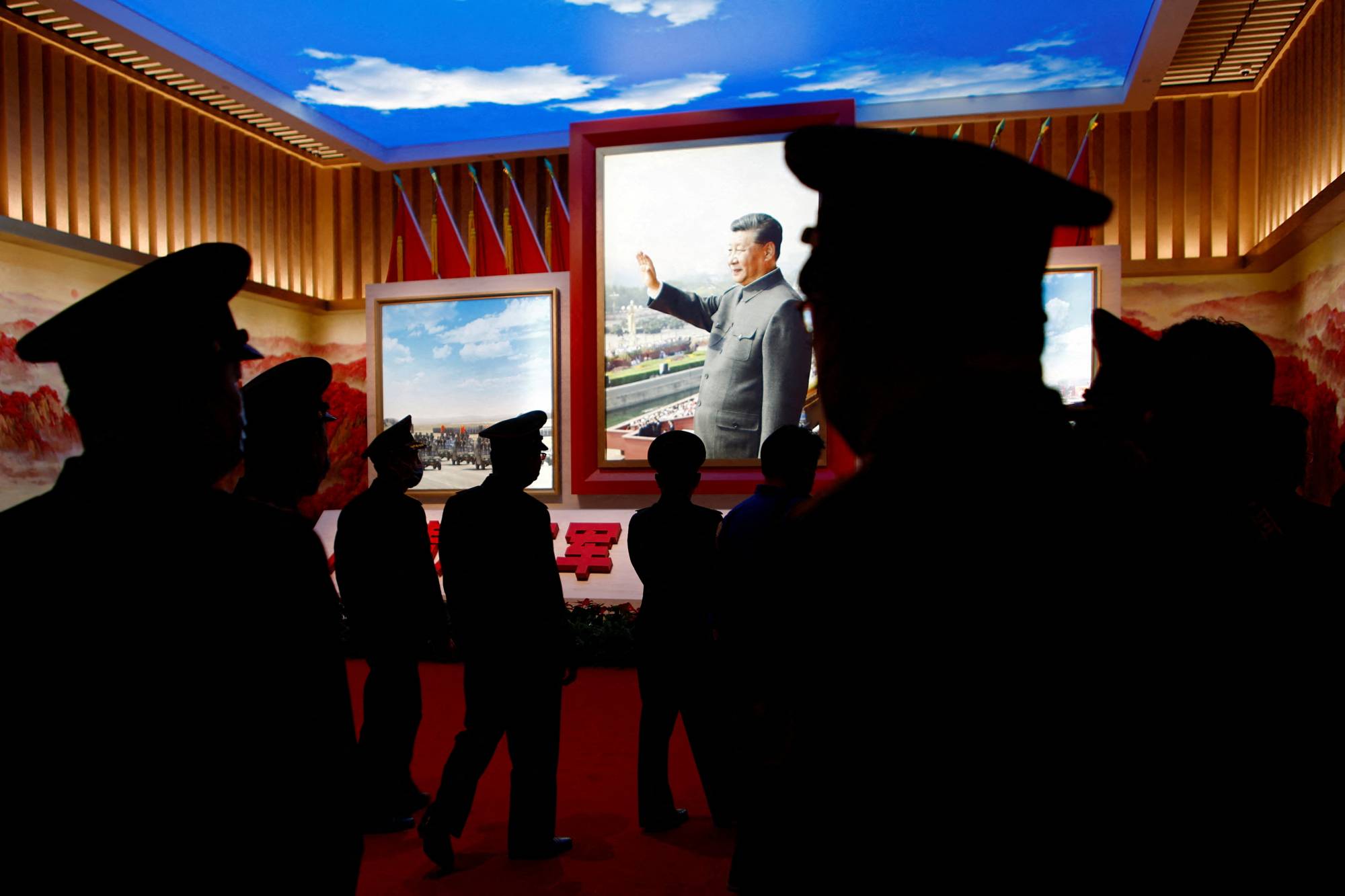 Chinese People's Liberation Army members walk past an image of Xi at an exhibition at the Military Museum in Beijing on Oct. 8. | REUTERS