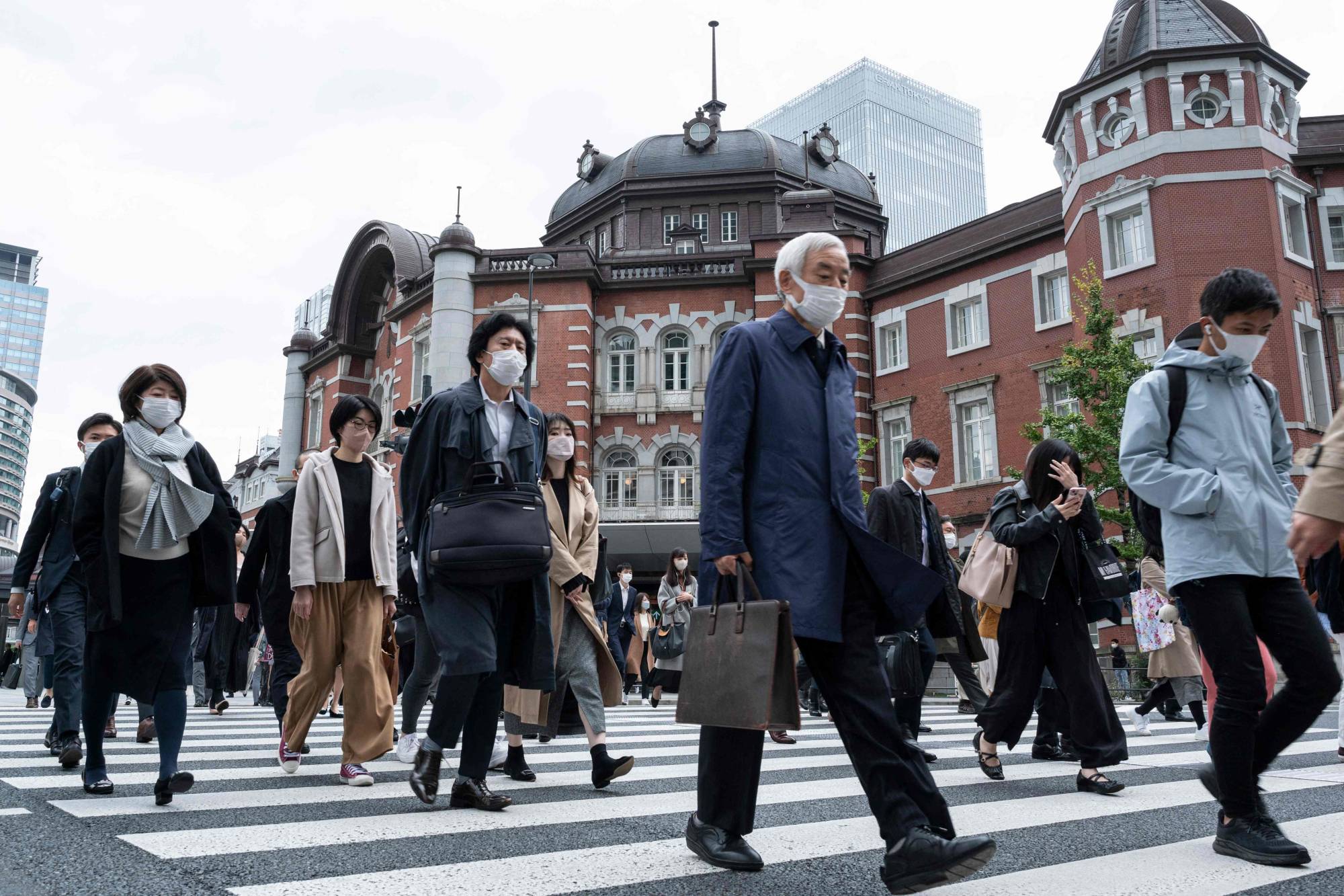 Travelers and commuters walk outside Tokyo Station on Friday. | AFP-JIJI