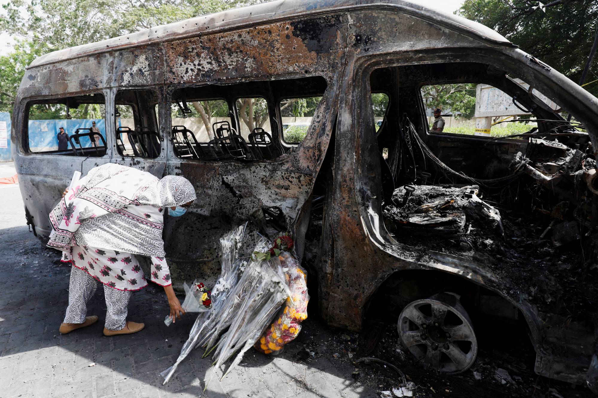 A student lays a bouquet in memory of her Chinese teachers near the wreckage of a passenger van outside the Confucius Institute at University of Karachi. | REUTERS
