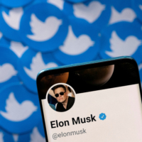 Elon Musk’s Twitter profile is seen on a smartphone placed against printed Twitter logos. | REUTERS