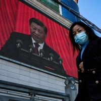 An outdoor screen displays a live speech of Chinese leader Xi Jinping from Beijing during the opening session of a rare Chinese Communist Party congress, as a pedestrian walks past in Yan\'an, China, on Oct. 16. | AFP-JIJI