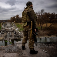 A Ukrainian serviceman stands guard at a destroyed bridge near Starytsya, Kharkiv region, on Saturday. | AFP-JIJI