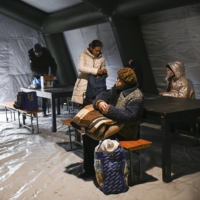 Ukrainians warm up in a heated tent with electricity to charge phones, in the main square of Kherson, Ukraine, on Friday. | LYNSEY ADDARIO / THE NEW YORK TIMES