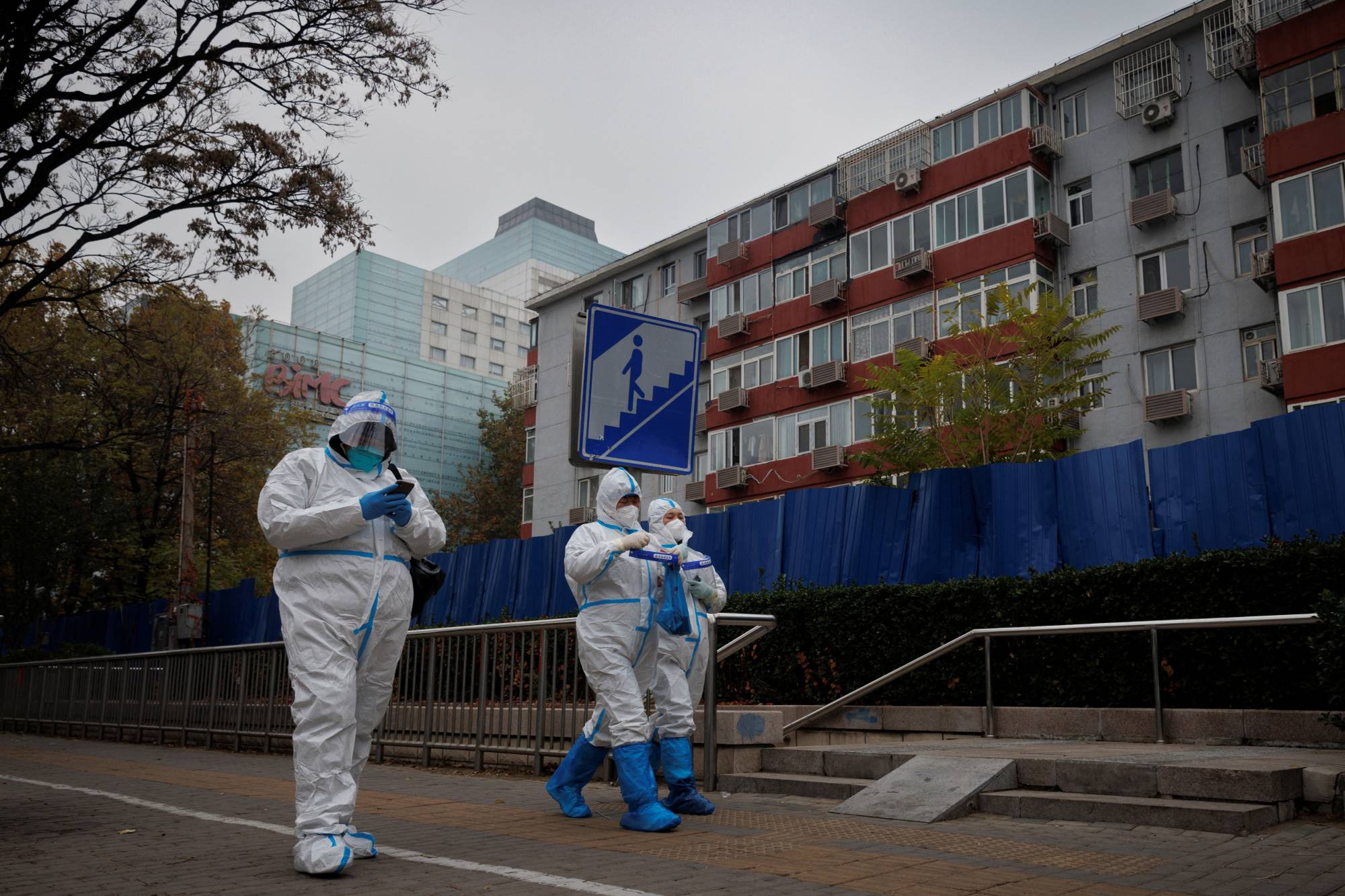 Pandemic prevention workers in protective suits walk outside a locked-down residential compound as outbreaks of COVID-19 continue in Beijing on Friday. | REUTERS