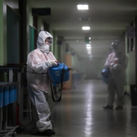 Workers spray disinfectant inside a hallway at Baekyoung high school in Anyang, South Korea, in December 2020. | BLOOMBERG 