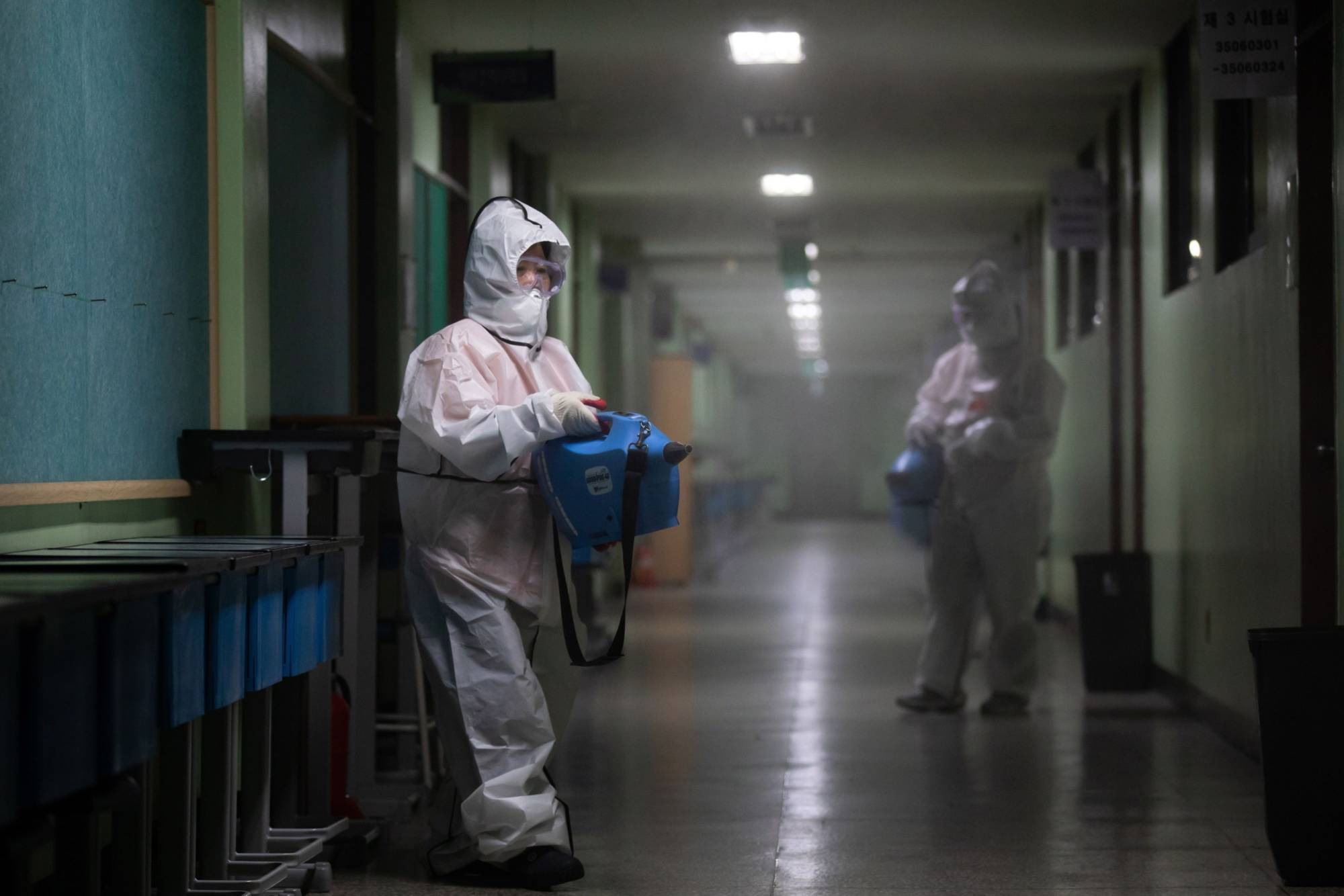 Workers spray disinfectant inside a hallway at Baekyoung high school in Anyang, South Korea, in December 2020. | Bloomberg 