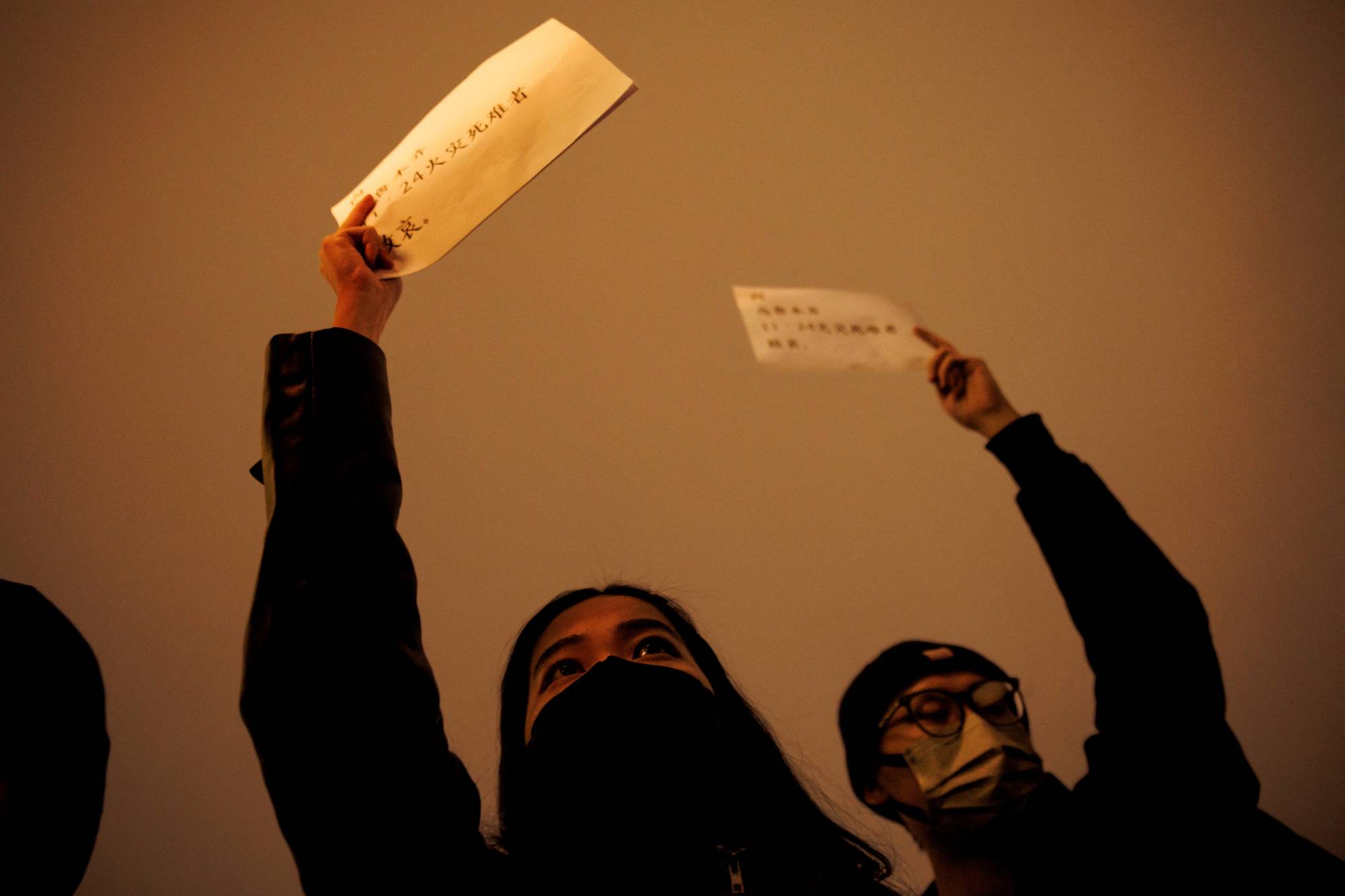 People gather for a vigil while holding blank sheets of paper in protest of strict 'COVID-zero' restrictions, in Beijing on Sunday. | REUTERS
