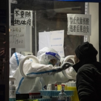 A worker in protective gear takes a swab sample at a COVID-19 testing facility in Shanghai on Friday night. | BLOOMBERG