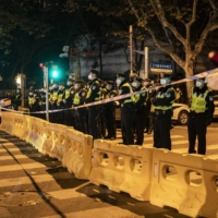 Police officers watch as protesters demonstrate against COVID-19 restrictions in Shanghai on Nov. 27. | THE NEW YORK TIMES