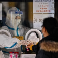A health worker prepares to take a swab sample from a woman to test for COVID-19 in the Jing\'an district in Shanghai on Thursday. | AFP-JIJI
