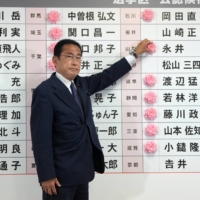 Prime Minister Fumio Kishida, also president of the Liberal Democratic Party, indicates a victory in the Upper House election by placing a pink paper rose next to an LDP candidate\'s name, at the party\'s headquarters in Tokyo on July 10. The ruling coalition secured a sweeping victory in the poll. | POOL / VIA REUTERS