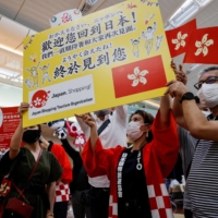 Members from shopping and tourism companies greet a group of tourists from Hong Kong upon their arrival at Haneda Airport in Tokyo on June 26. Japan gradually eased its strict COVID-19 border controls over the year, finally letting in all arrivals from Oct. 11. | REUTERS