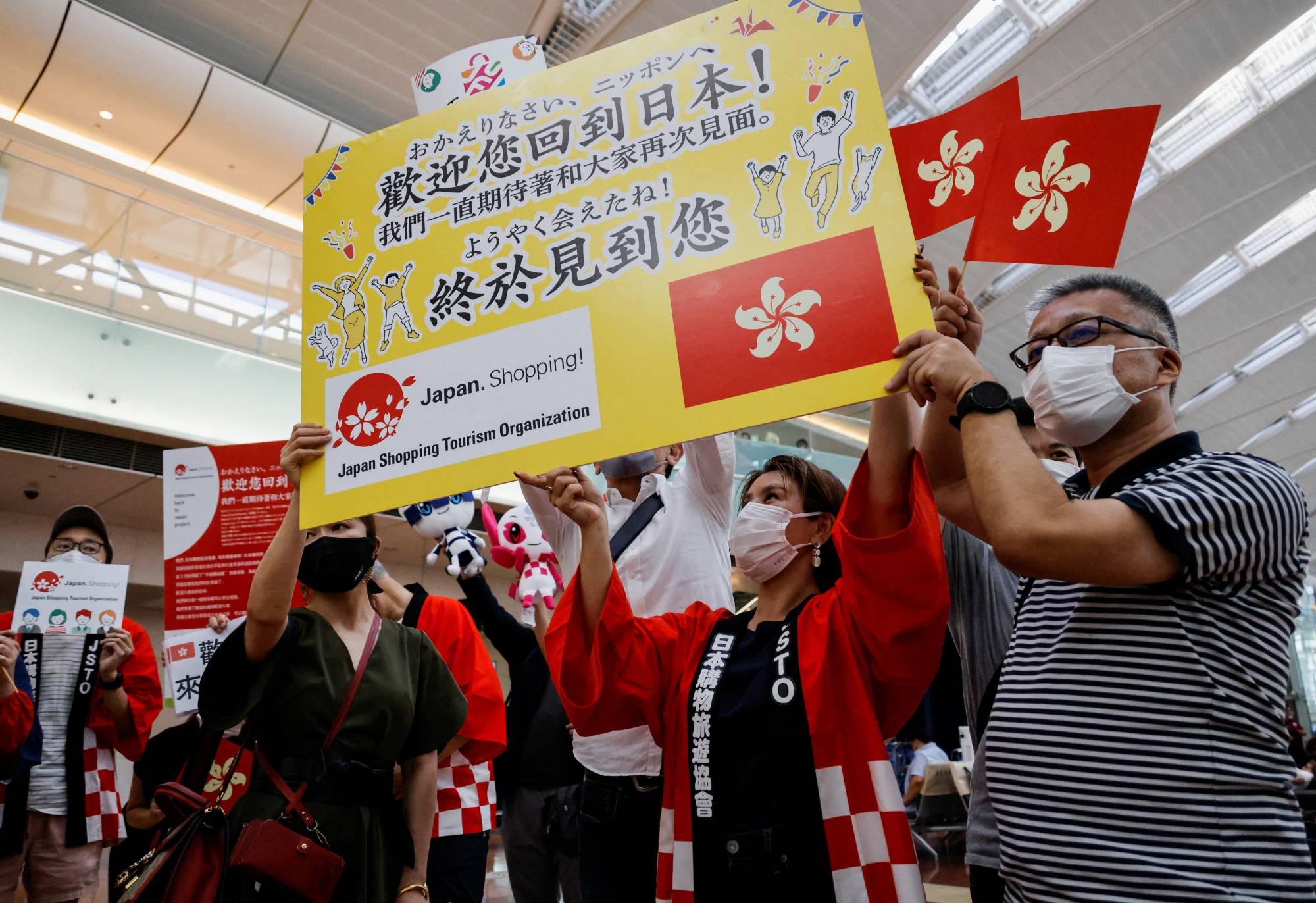 Members from shopping and tourism companies greet a group of tourists from Hong Kong upon their arrival at Haneda Airport in Tokyo on June 26. Japan gradually eased its strict COVID-19 border controls over the year, finally letting in all arrivals from Oct. 11. | REUTERS