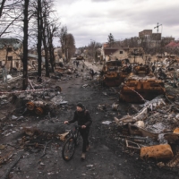 A man passes debris and destroyed Russian military vehicles on a street in Bucha, Ukraine, in April. | CHRIS MCGRATH / GETTY IMAGES