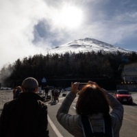 Tourists take photographs of Mount Fuji during a bus tour in Fujiyoshida, Yamanashi Prefecture, in November. | BLOOMBERG