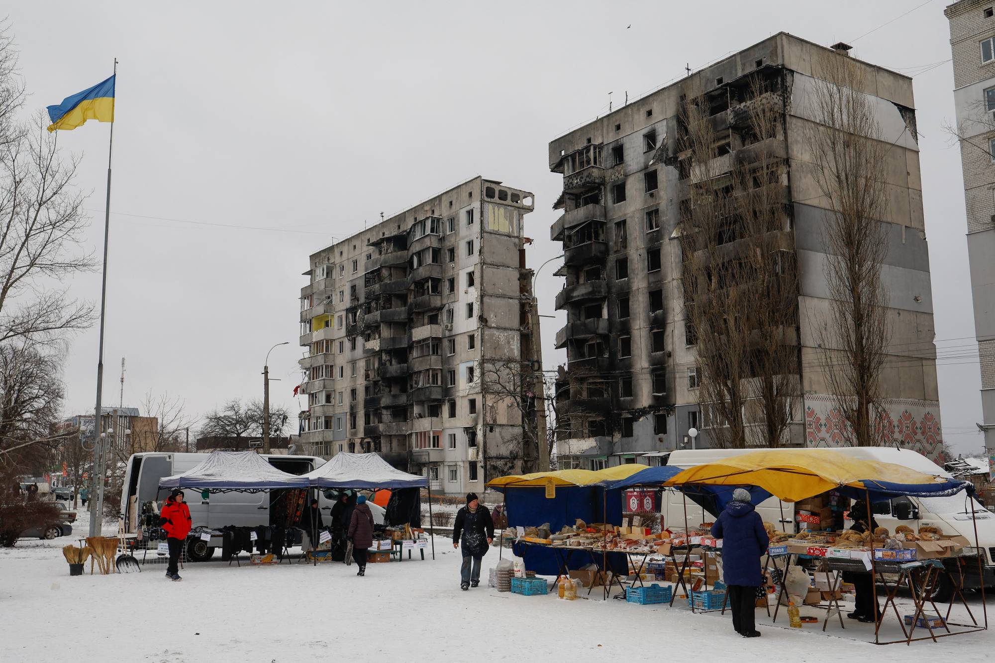 Residents buy food at a street market in front of buildings damaged by Russian strikes, in Borodianka, Ukraine, on Dec. 15. | Reuters 