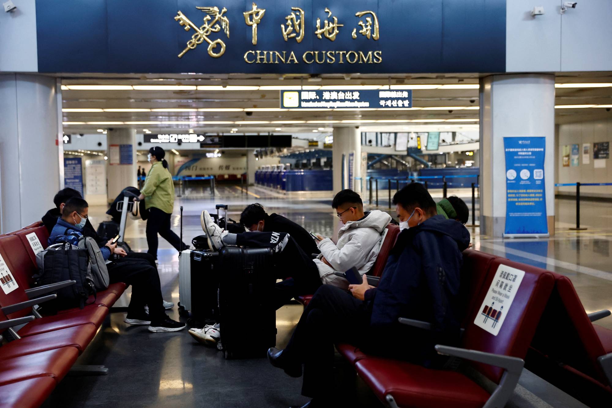 Travelers wait with their luggage at Beijing Capital International Airport in Beijing on Tuesday. | REUTERS