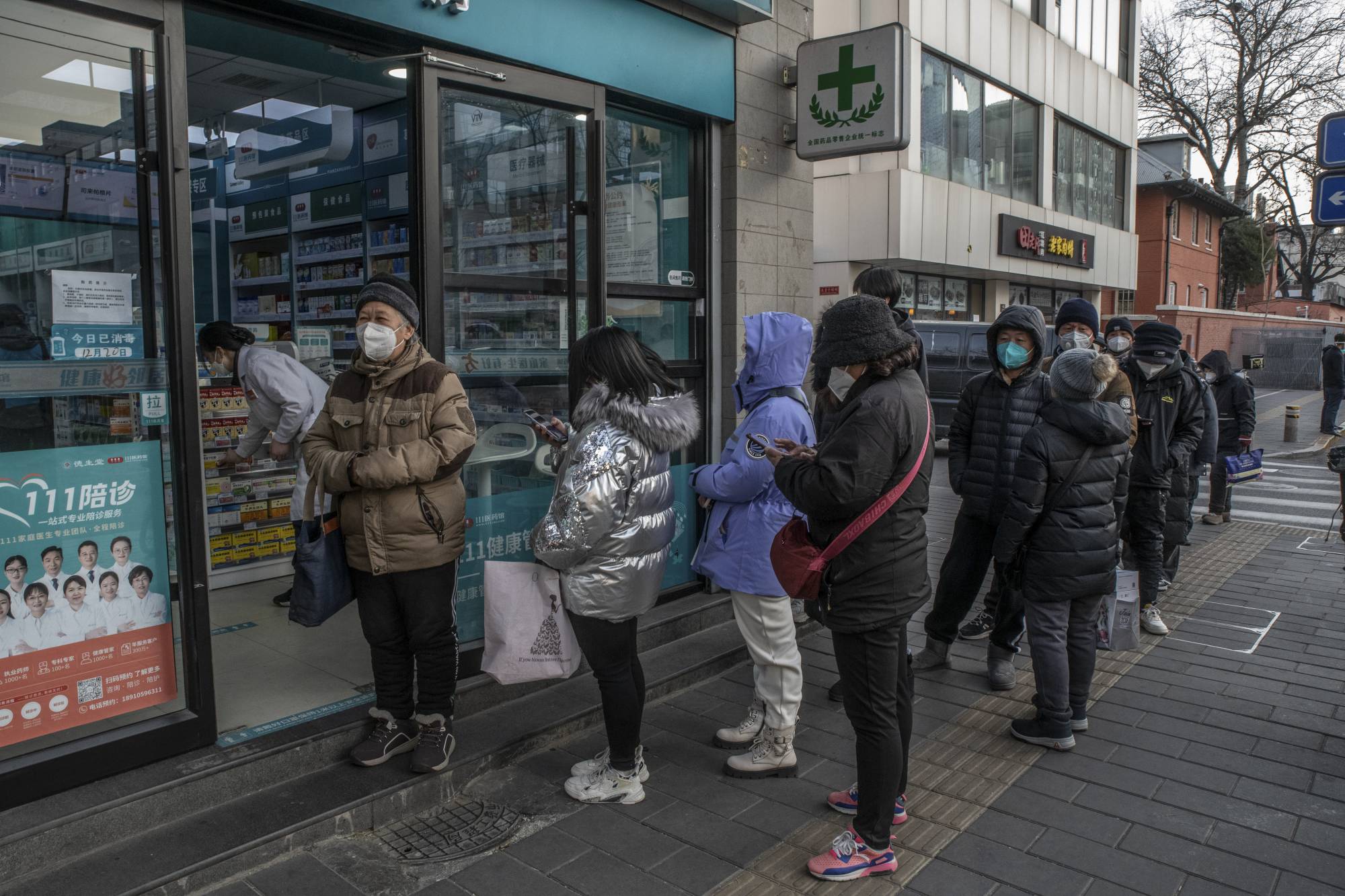 People stand in line outside a pharmacy in Beijing. A surge of infections has prompted shortages of fever-reducing medicines.  | GILLES SABRIE / THE NEW YORK TIMES