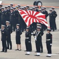 Self-Defense Force service members stand with the naval flag prior to a review ceremony on a runway at the Air Self-Defense Force\'s Hyakuri Air Base in Omitama, Ibaraki Prefecture, in October 2014. | AFP-JIJI