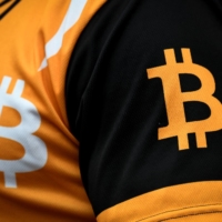 A man wears a t-shirt with the logo of bitcoin as he waits for Sam Bankman-Fried, the founder and former CEO of cryptocurrency exchange FTX, to attend a hearing at the Magistrate Court building in Nassau, Bahamas, on Dec. 19. | REUTERS