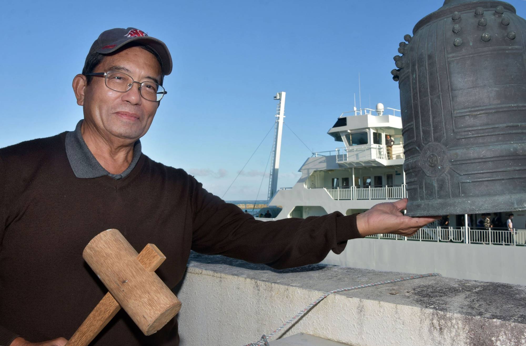 Shizuo Kishaba shows a bronze bell that was returned from the U.S. and set up at a port in Iheya, Okinawa Prefecture, on Nov. 28. | NISHINIPPON SHIMBUN