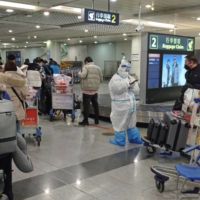 Passengers arriving on international flights wait next to a staff member at the airport in Chengdu, China, on Friday.  | REUTERS