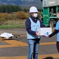 A delivery staff member hands a parcel to a drone staffer. | Seino Holdings