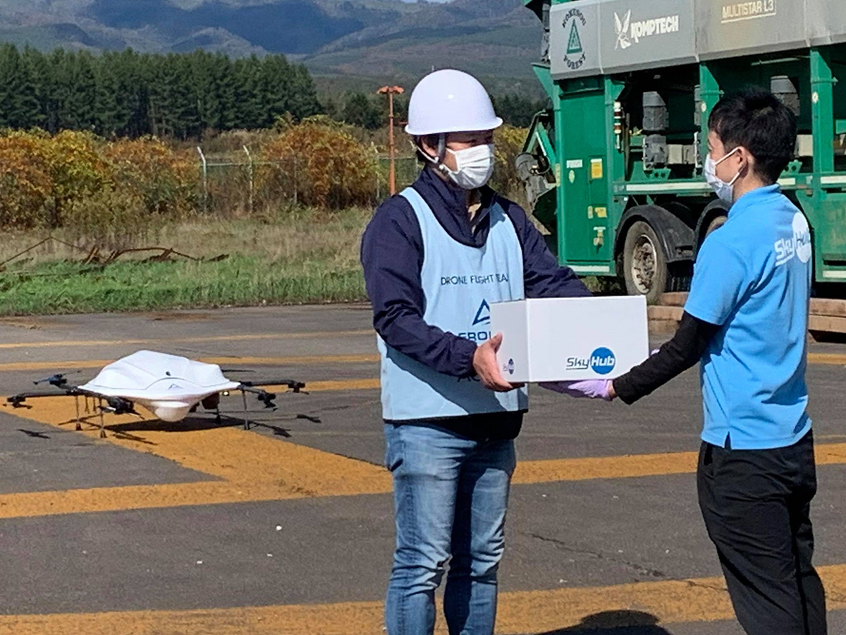 A delivery staff member hands a parcel to a drone staffer. | Seino Holdings