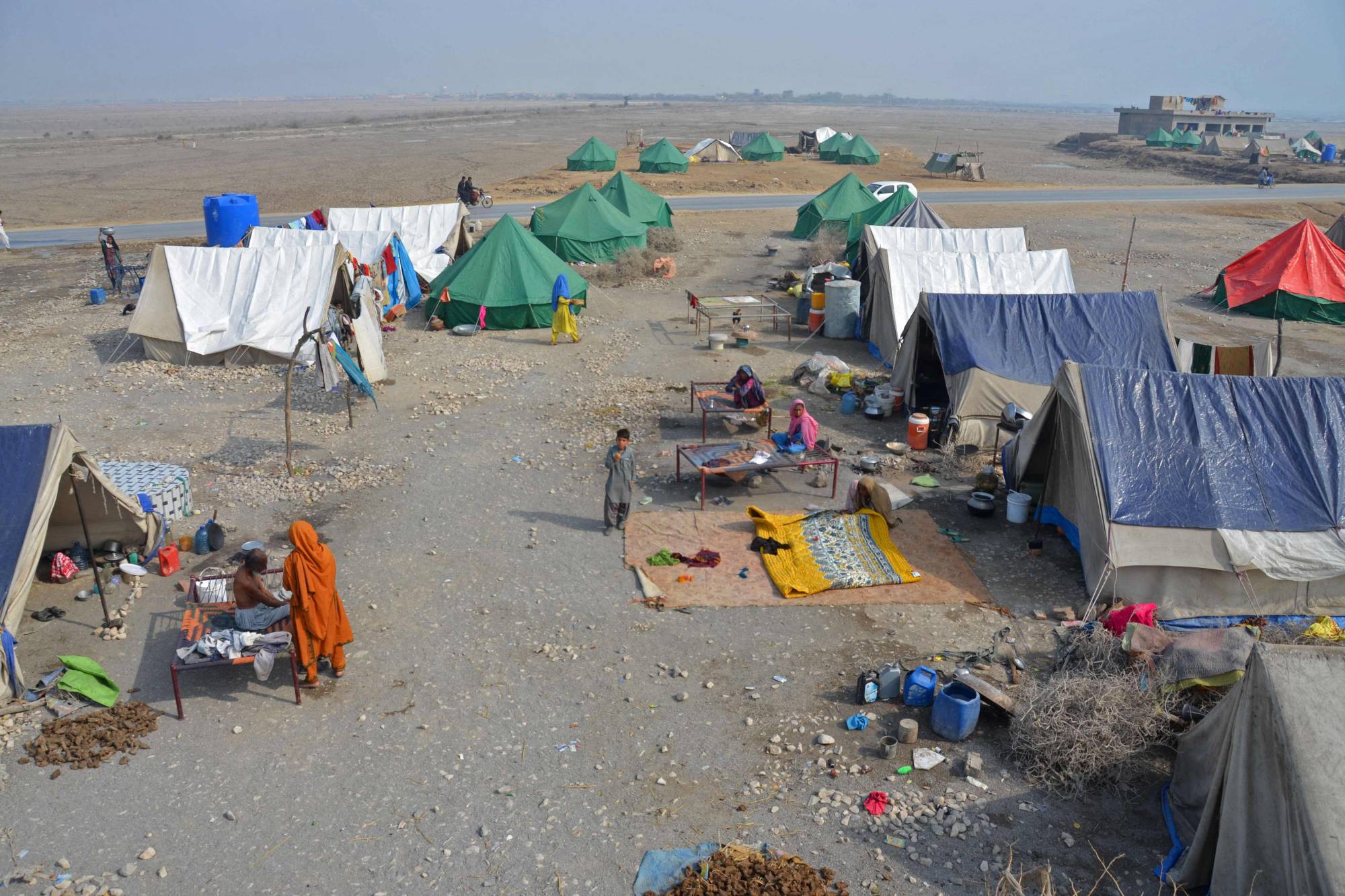 Internally displaced flood-affected people sit around a makeshift camp in the area of Dera Allah Yar on Jan. 9. | AFP-Jiji