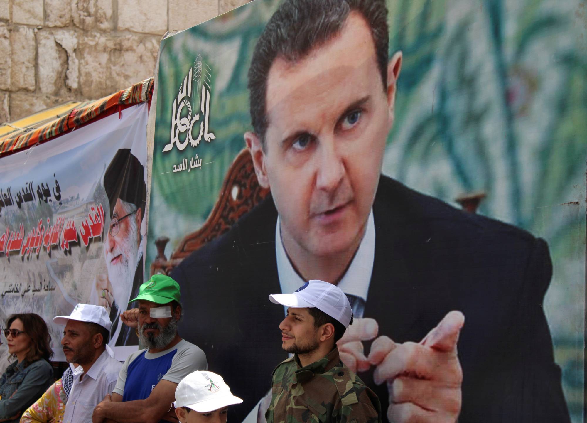 Syrians and Palestinians living in Syria stand next to a poster depicting Syria's President Bashar al-Assad as they mark the annual al-Quds Day (Jerusalem Day), in Damascus, Syria, in April last year. | REUTERS