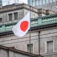 The Japanese national flag is seen at the Bank of Japan headquarters in Tokyo on Tuesday. Given that the next governor will be under pressure to disentangle and review the BOJ\'s complex ultraloose monetary policy, someone with a neutral stance like Ueda is seen as being more appropriate for the job. | AFP-JIJI