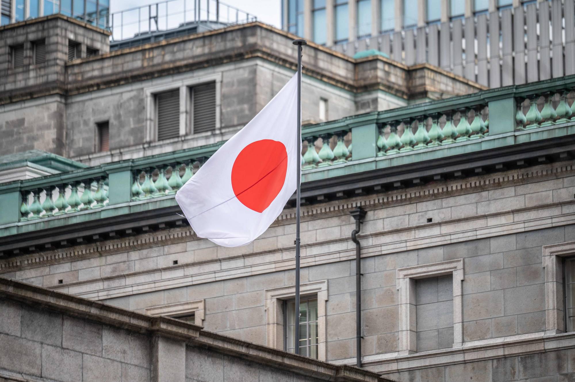 The Japanese national flag is seen at the Bank of Japan headquarters in Tokyo on Tuesday. Given that the next governor will be under pressure to disentangle and review the BOJ's complex ultraloose monetary policy, someone with a neutral stance like Ueda is seen as being more appropriate for the job. | AFP-JIJI