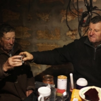 Stepan Kovalyov, 80 (left) and his brother Volodymyr Kovalyov, 77, toast with horilka — a Ukrainian spirit — inside of a cellar where Stepan and his wife live after their house was destroyed during the Russian occupation, in the village of Posad-Pokrovske, Ukraine. | REUTERS