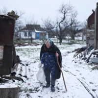 Tetiana Kovalyova, 76, carries a bag of firewood for the wood-burning stove, which is used to heat the only room in their house that still has a roof | REUTERS