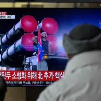 Passers-by watch a television showing a news broadcast with file footage of a North Korean military parade, at the main railway station in Seoul on Monday. | AFP-JIJI