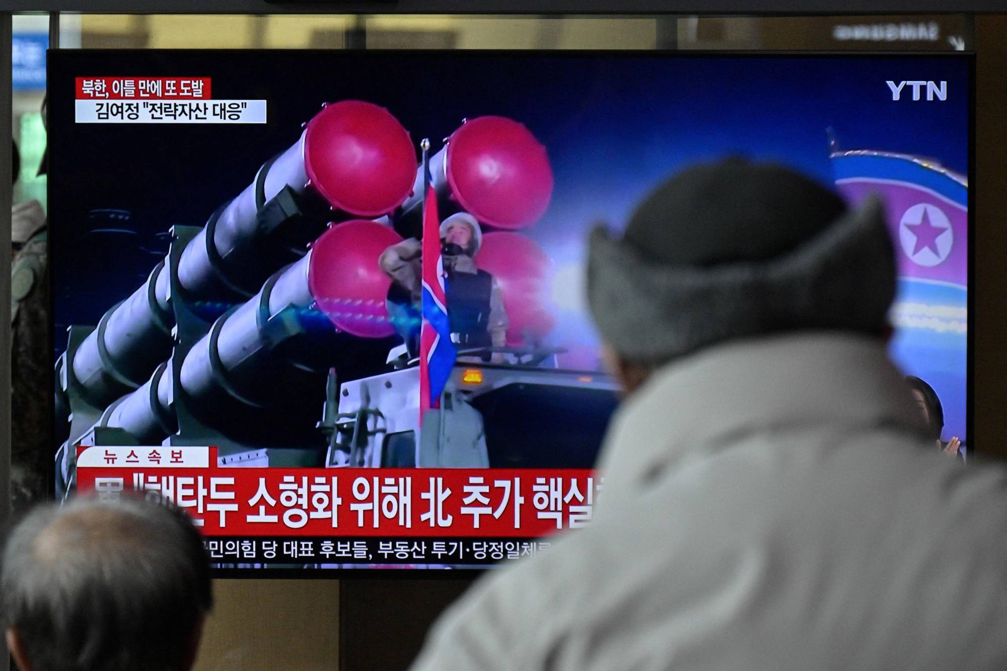 Passers-by watch a television showing a news broadcast with file footage of a North Korean military parade, at the main railway station in Seoul on Monday. | AFP-JIJI