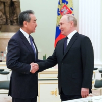Russia\'s President Vladimir Putin shakes hands with China\'s Director of the Office of the Central Foreign Affairs Commission Wang Yi during a meeting in Moscow on Wednesday. | SPUTNIK / POOL / VIA REUTERS