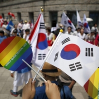 A participant holds up a rainbow and a South Korean national flag as they face Christian groups against homosexuality, during the Korea Queer Festival in Seoul on June 28, 2015.  | REUTERS