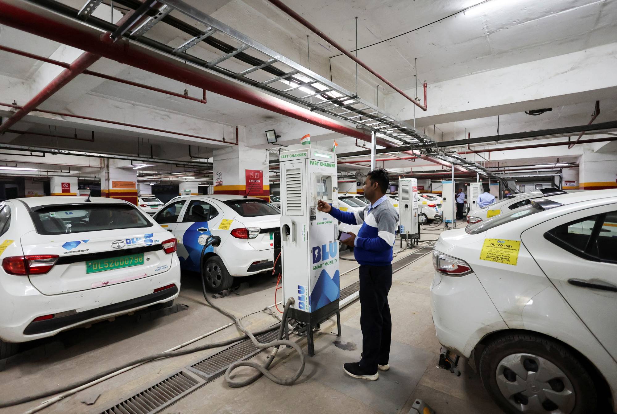 A man charges an electric vehicle (EV) at the charging hub of Indian ride-hailing BluSmart Electric Mobility in Gurugram, India, on Dec. 9. | REUTERS