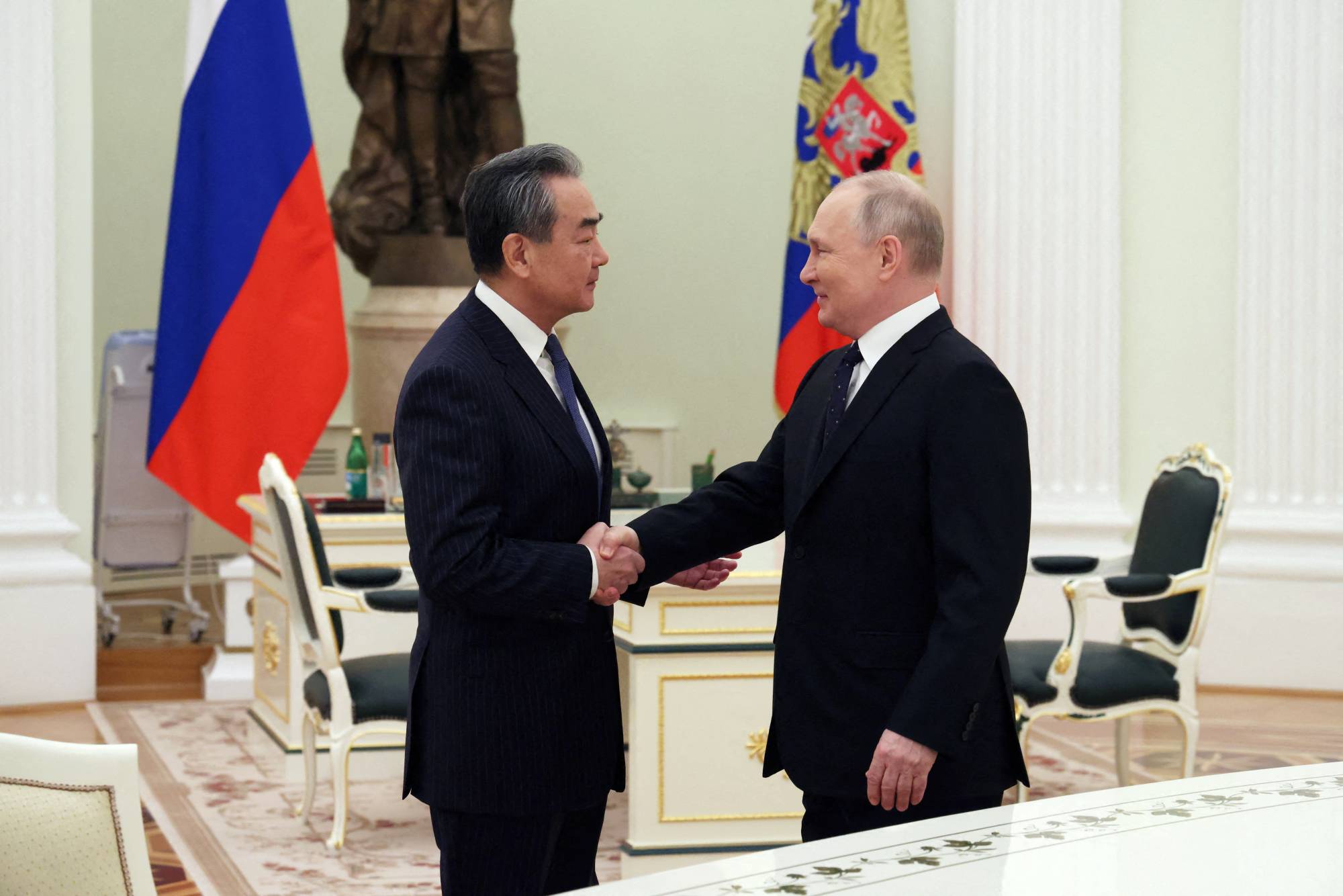 Russian President Vladimir Putin shakes hands with Wang Yi, China's top diplomat, during a meeting in Moscow on Wednesday. | Pool / Sputnik / via REUTERS