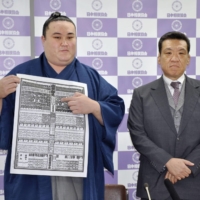 Newly promoted maegashira Kinbozan, joined by Kise stablemaster, points to his name in the latest banzuke rankings during a news conference at Ryogoku Kokugikan on Monday. | KYODO