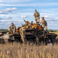 Four soldiers, volunteers from the U.S. and the U.K., stand on a tank they took down on the Izium front in Ukraine. | SAPHRYN SHIKAZE