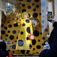 People watch as a lifelike robot of Yayoi Kusama paints polka dots on the window of the luxury retailer Louis Vuitton store in Paris. | REUTERS