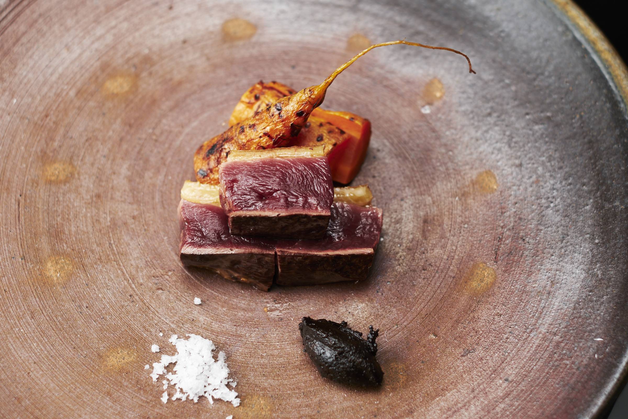 Chef Haruki Sato grills wild duck breast together with charcoal-grilled carrots that have been harvested from under the deep snow. | KOUTAROU WASHIZAKI 
