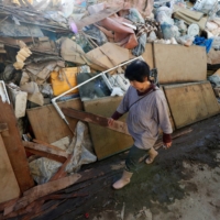 A woman walks past debris in the aftermath of Typhoon Hagibis in the city of Date, Fukushima Prefecture, in October 2019. Japan expects more severe typhoons and as much as 1.5 times more rainfall by the end of the century, both of which will increase the risk of flooding. | REUTERS