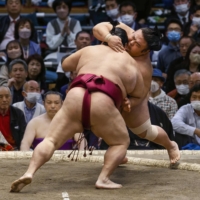 Takakeisho (back right) is pushed out of the ring by Mitakeumi at the Edion Arena Osaka on Friday. | KYODO
