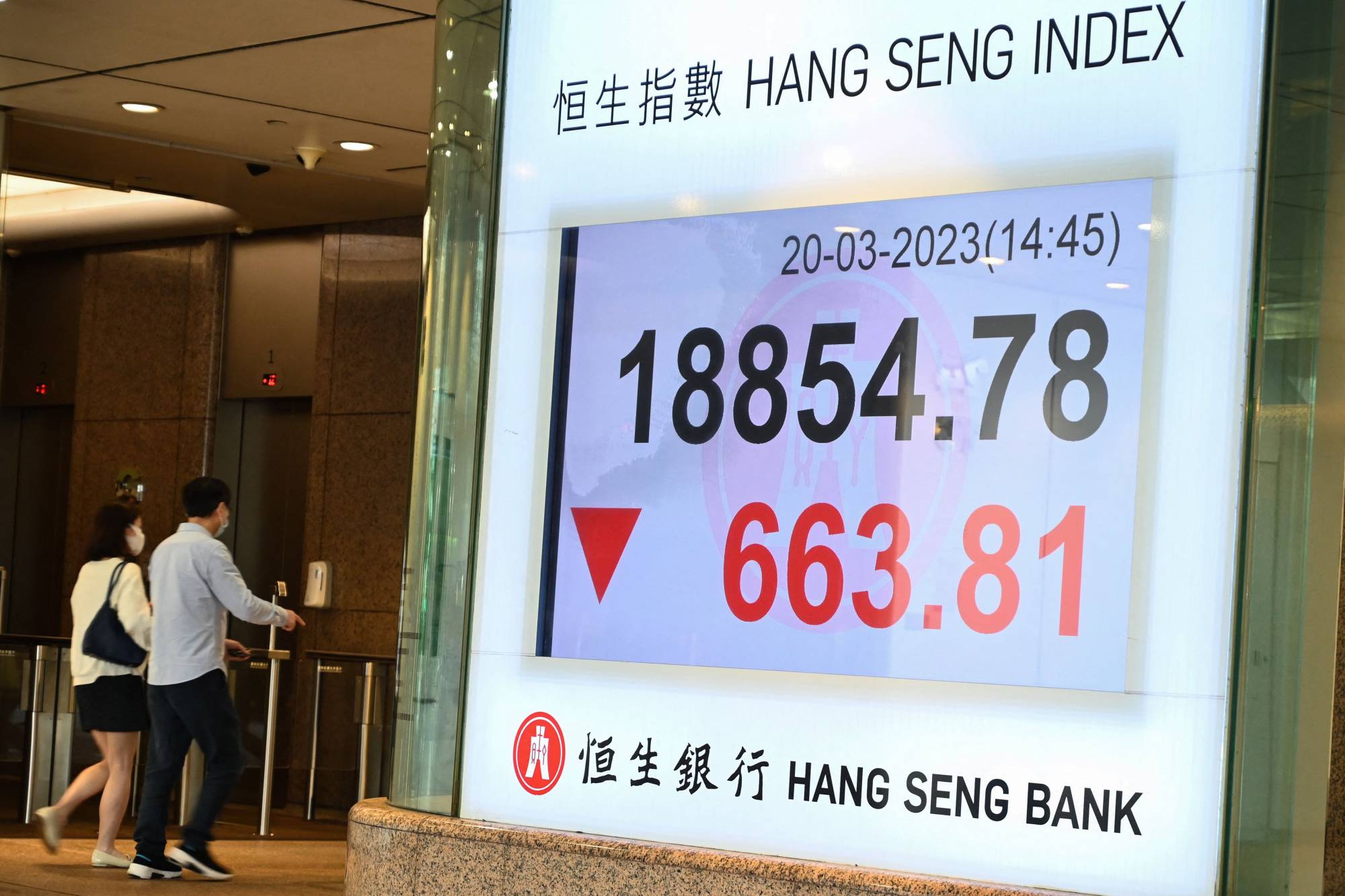 People walk past a sign showing the numbers for the Hang Seng Index in Hong Kong on Monday. | AFP-JIJI